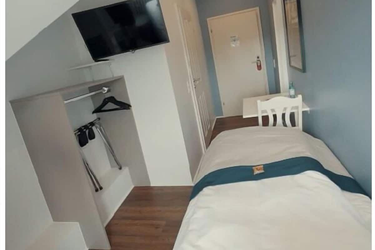 Een slaapkamer met een bed, een aan de muur bevestigde televisie, een kapstok en een klein tafeltje.