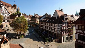A historic town square with traditional half-timbered buildings, cobblestone streets, and a prominent tower. - Hotel Metropol Nürnberg (Nuremberg)