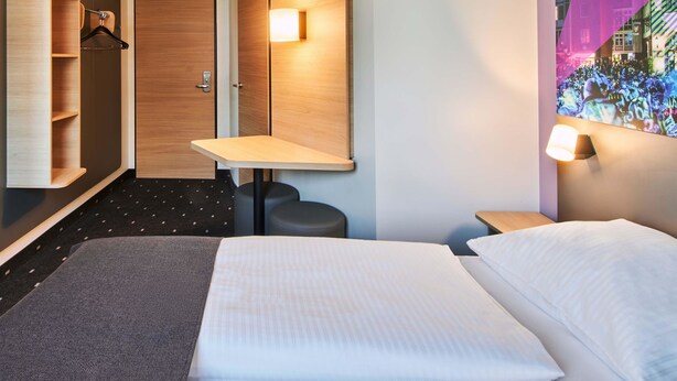 A hotel room with a bed, a desk, a chair, a wardrobe, and a mirror. - B&B Hotel Frankfurt-Niederrad (Frankfurt)