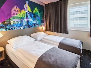 A hotel room with two beds, a large window with curtains, a wall-mounted TV displaying a cityscape, and a nightstand with a lamp. - B&B Hotel Frankfurt-Niederrad (Frankfurt)
