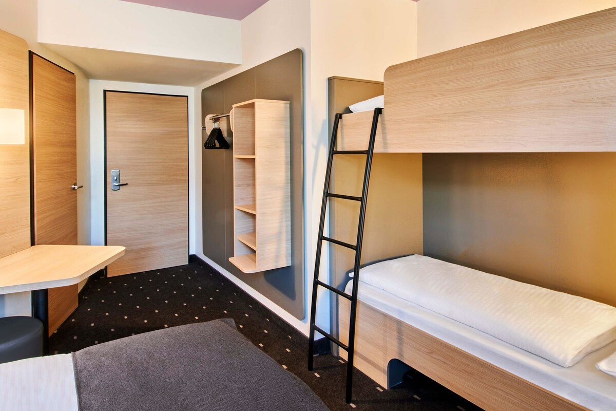 A compact hotel room with a bunk bed, a desk, and a wardrobe.