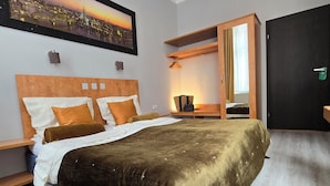 A hotel room with a bed, a nightstand, a wooden wardrobe, a framed cityscape picture, and a window with curtains. - City Hotel Storch (Cologne)