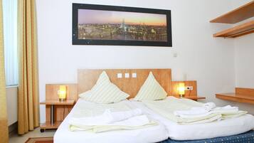 A hotel room with a bed, two bedside tables with lamps, a framed cityscape picture on the wall, and a window with curtains.