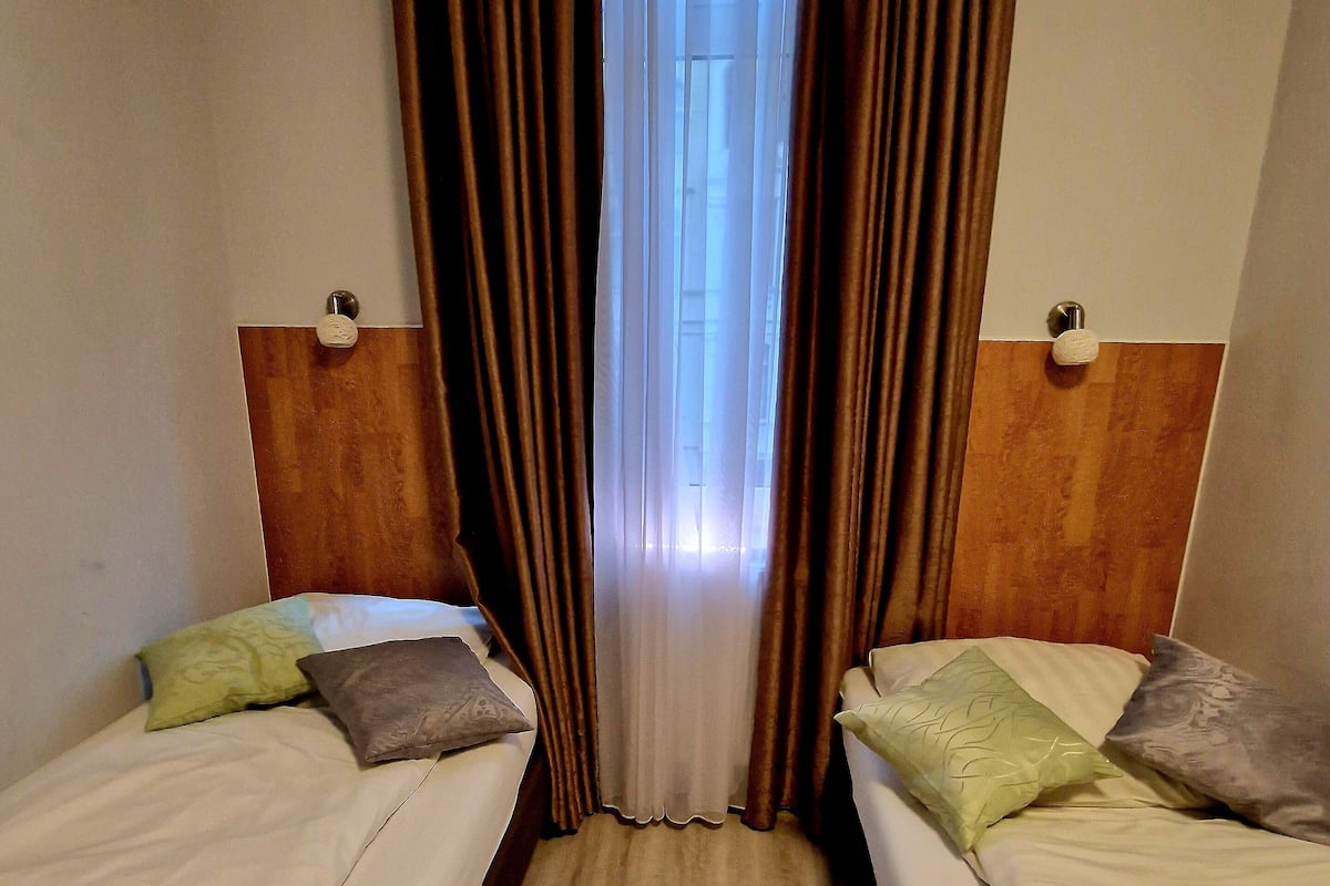 A hotel room with two single beds, a wooden floor, and a window with curtains.