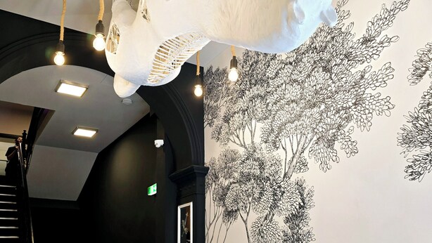 A hallway with a black and white checkered floor, a staircase, and a wall mural of trees. - City Hotel Storch (Cologne)