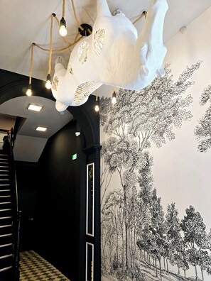 Ein Flur mit kariertem Schwarz-Weiß-Boden, einer Treppe und einem Wandbild von Bäumen.