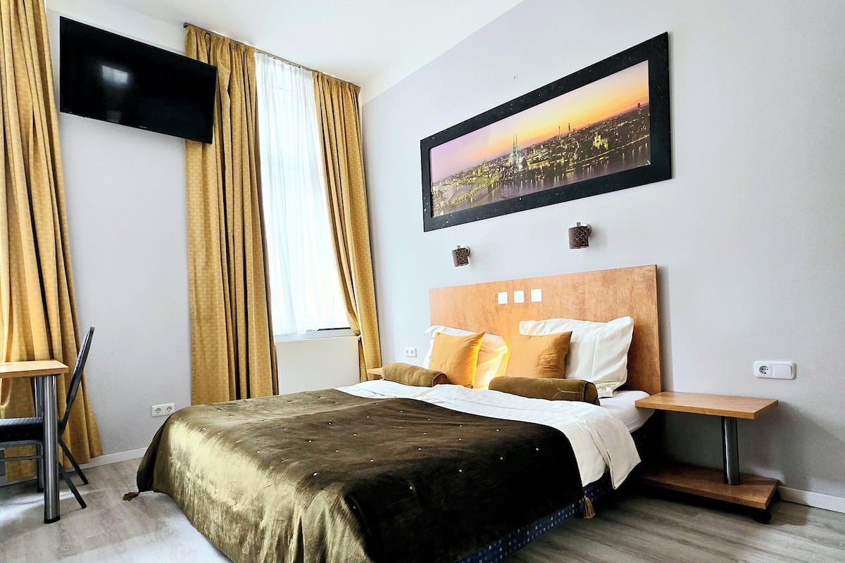 A hotel room with a bed, a TV mounted on the wall, a framed picture, and a small table.