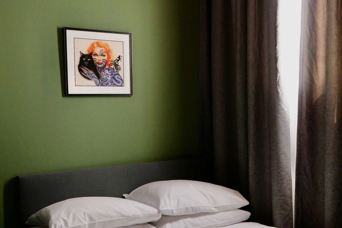 Una cama con ropa blanca, un cuadro en la pared y una ventana con cortinas.