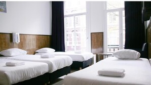 A hotel room with three beds, a window with a view of buildings, and a small table with a chair. - Hotel Kap (Amsterdam)