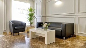 A modern lobby with a black leather sofa, a white coffee table, and a potted plant. - Bonanova Suite Hotel (Barcelona)