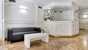 A modern lobby with a black leather sofa, a white bench, and a decorative plant. - Bonanova Suite Hotel (Barcelona)