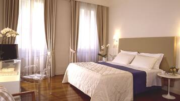 Habitación de hotel con cama, escritorio, computadora, silla y una pequeña mesa con un jarrón de flores.