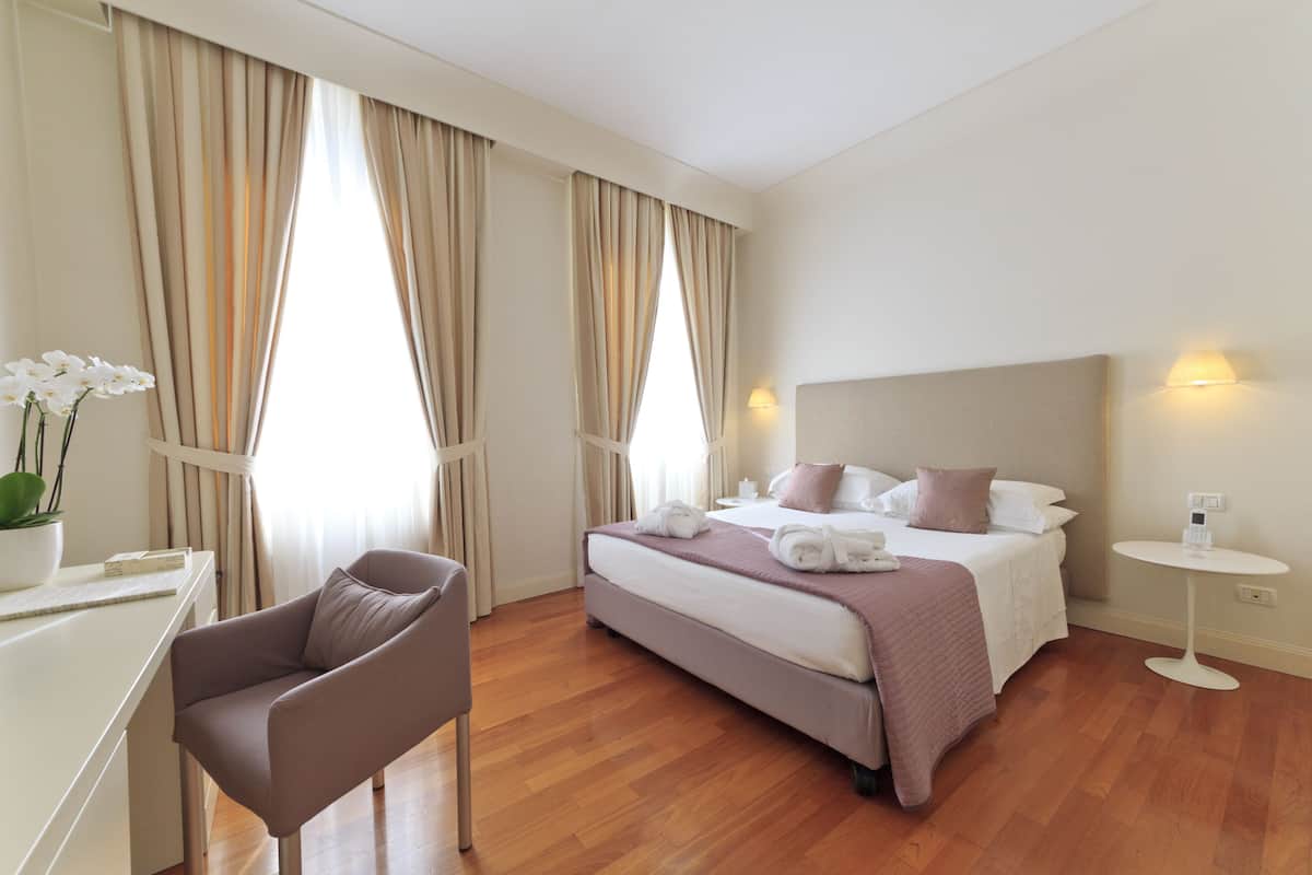 A hotel room with a bed, bedside table, chair, and curtains.