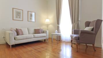 A living room with a sofa, armchair, lamp, and framed pictures on the wall.