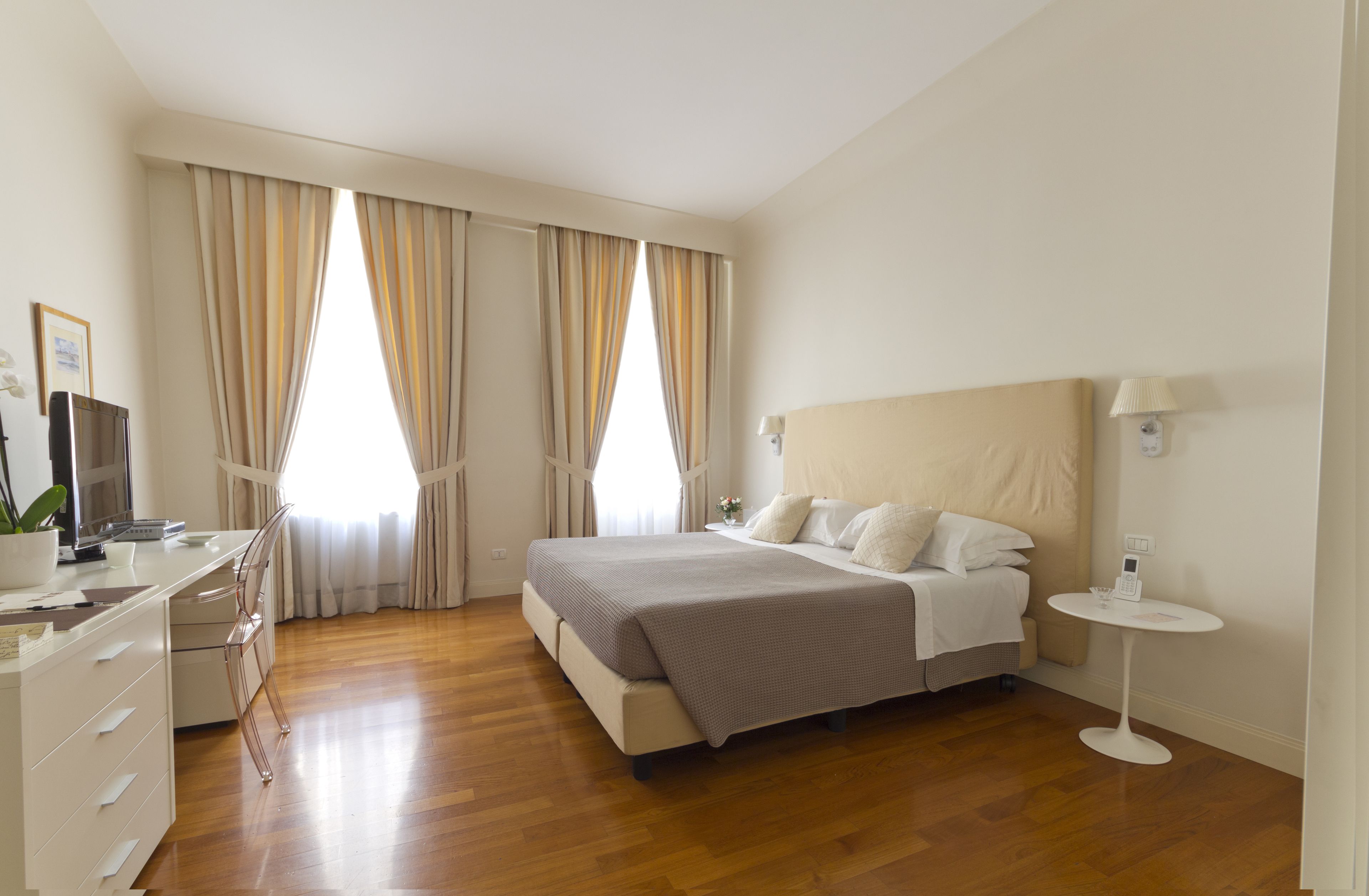 A modern bedroom with a large bed, bedside tables, a desk, and a chair.