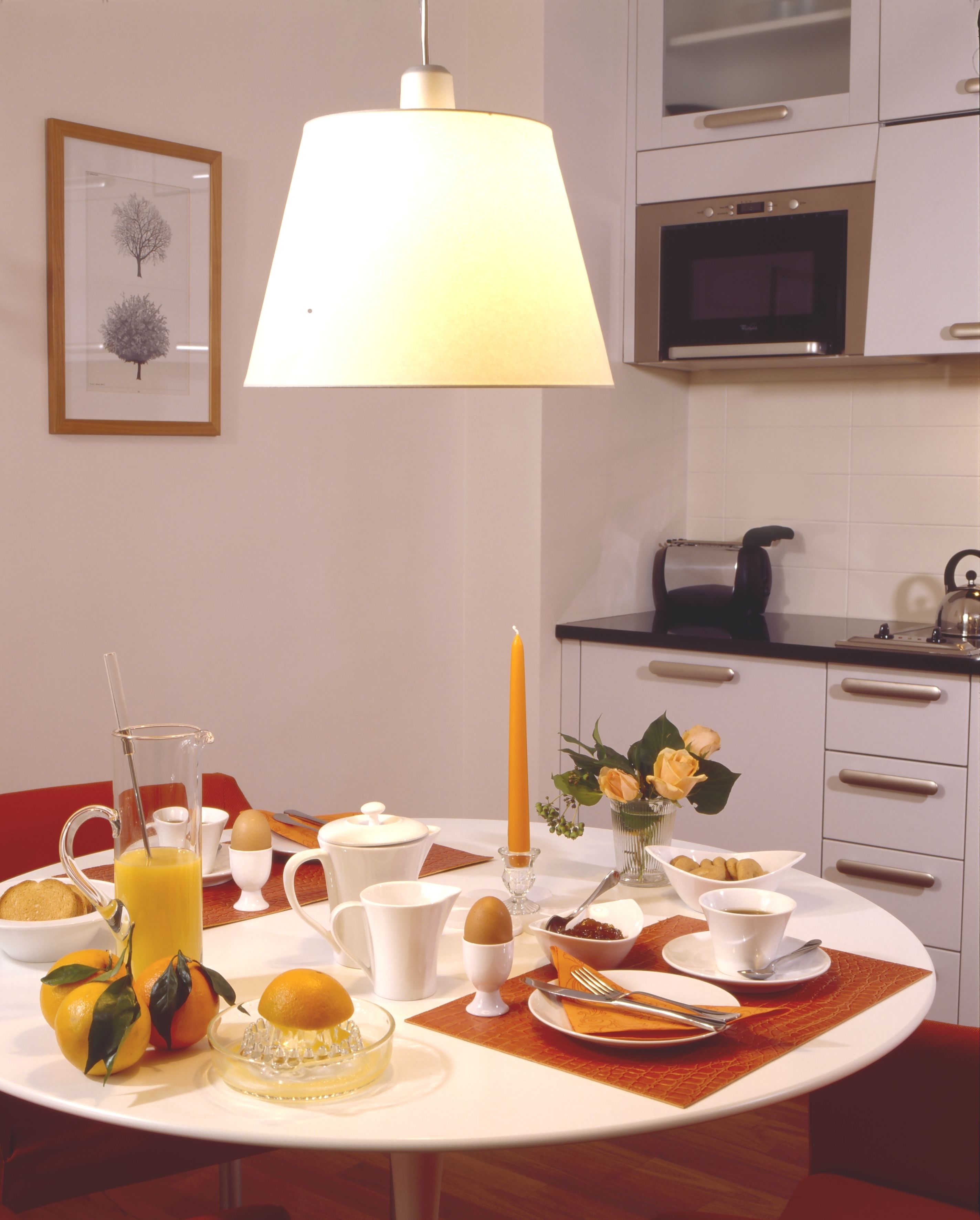 A breakfast setting with a table set for two, including a pitcher of orange juice, a candle, and a vase with flowers.