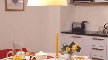 A breakfast setting with a table set for two, including a pitcher of orange juice, a candle, and a vase with flowers.