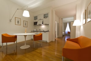 A modern living room with a wooden floor, a white round table, two orange chairs, and a sofa.