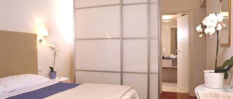 A hotel room with a bed, a sliding door, a nightstand with a lamp, and a potted orchid.
