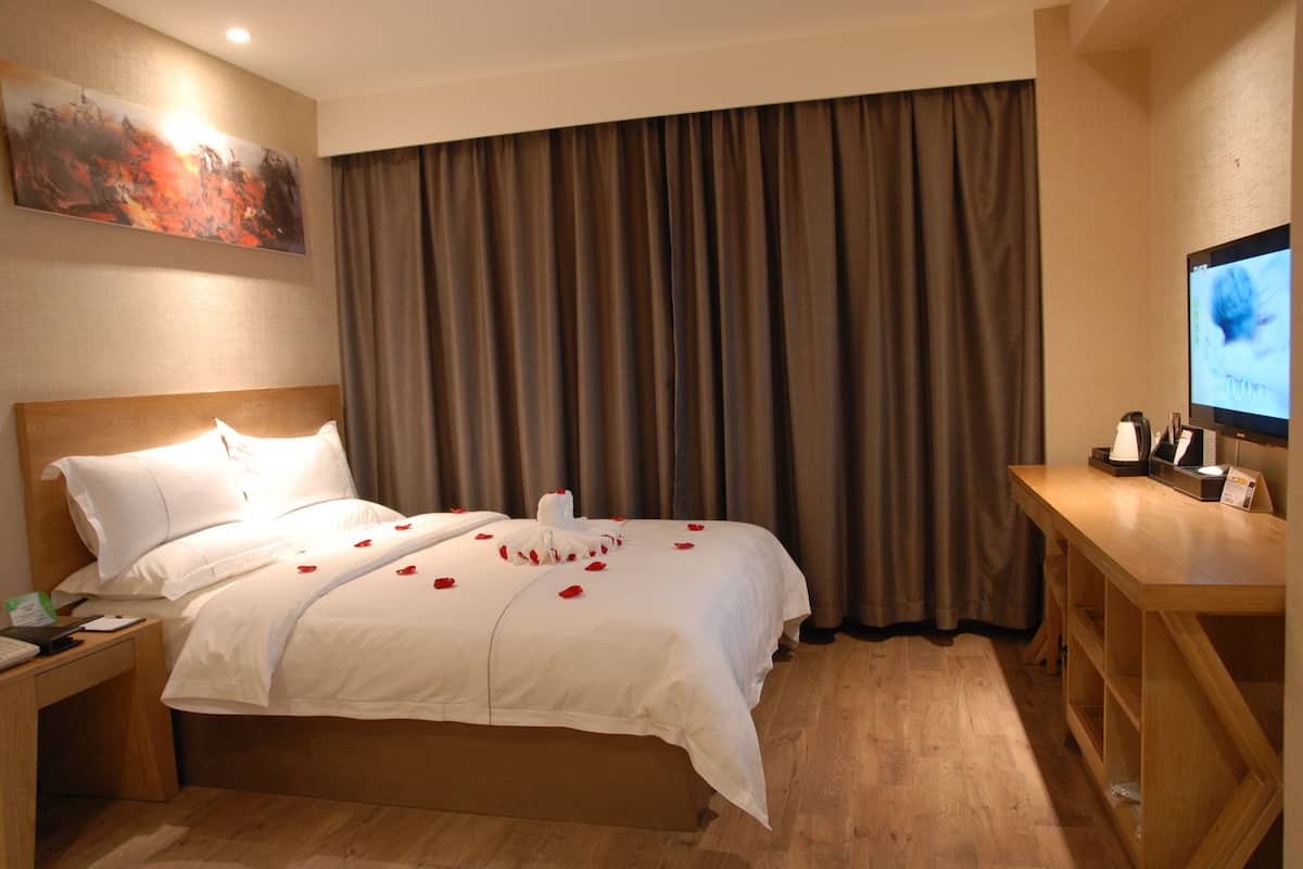 A hotel room with a large bed, a wooden desk, a television, and a painting on the wall.