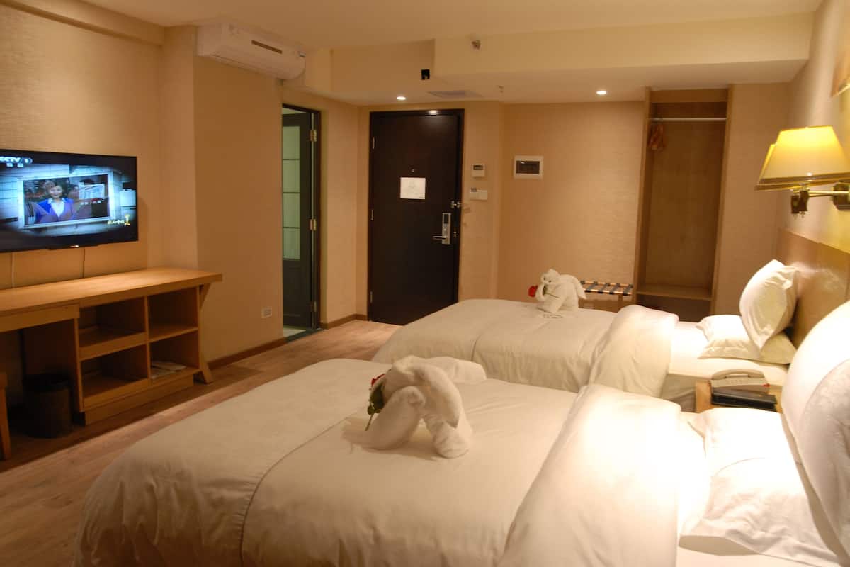 A hotel room with two beds, a TV on the wall, a desk, and a door.