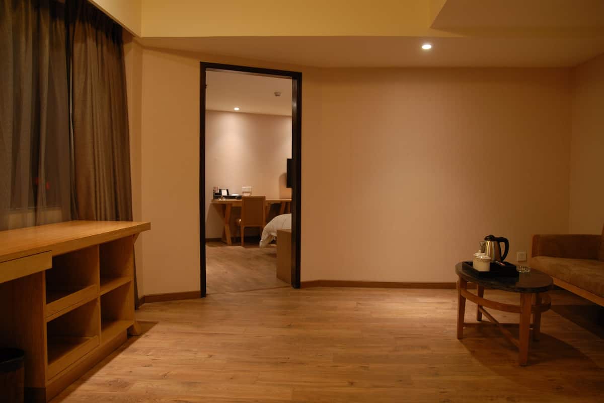A room with a wooden desk, a small table with a kettle, a sofa, and a mirror reflecting a dining area.