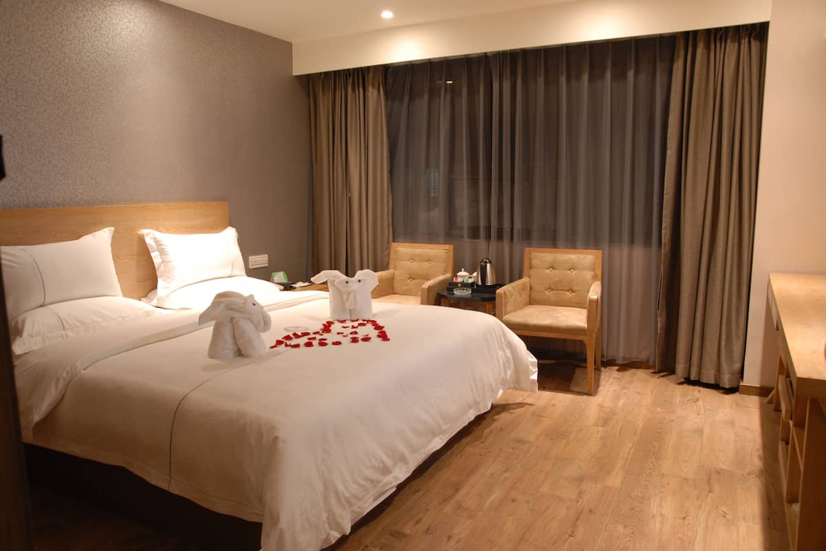 A hotel room with a large bed, two armchairs, a small table, and a window with curtains.
