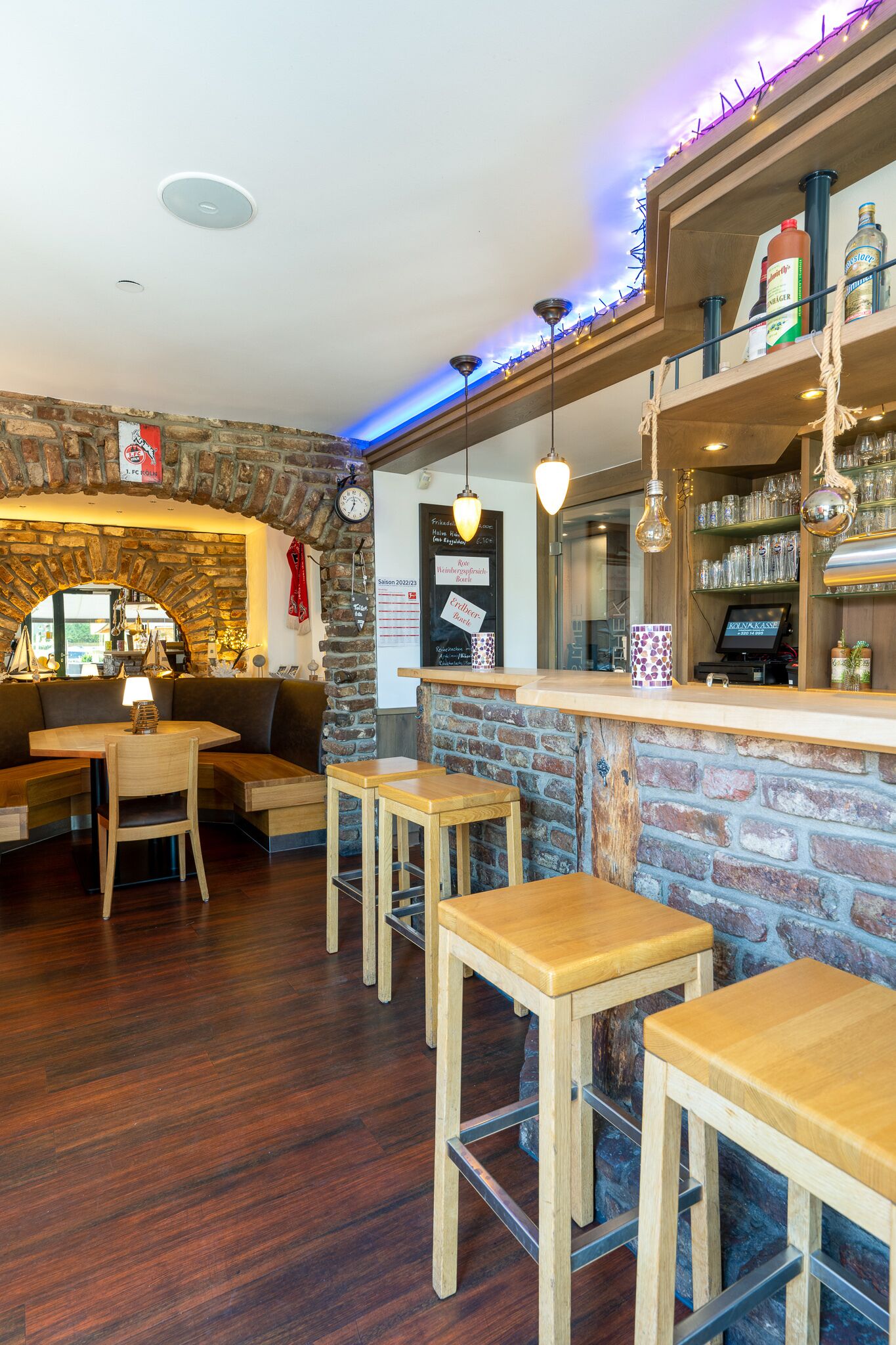 Angolo accogliente di un bar con sgabelli di legno, un arco in pietra e un bancone pieno di bottiglie e bicchieri.
