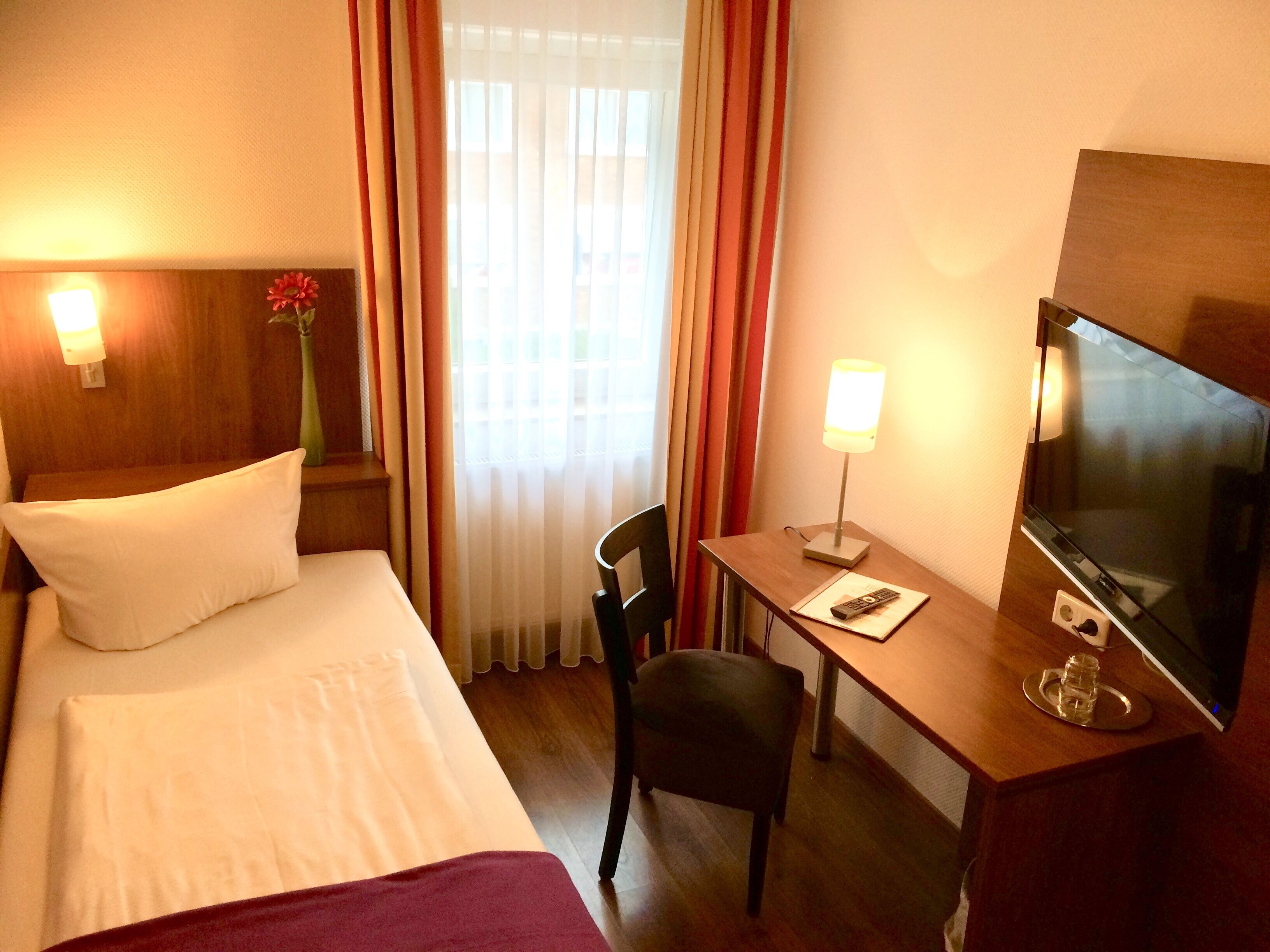 Una habitación de hotel con una cama, un escritorio, una silla, un televisor y una lámpara.