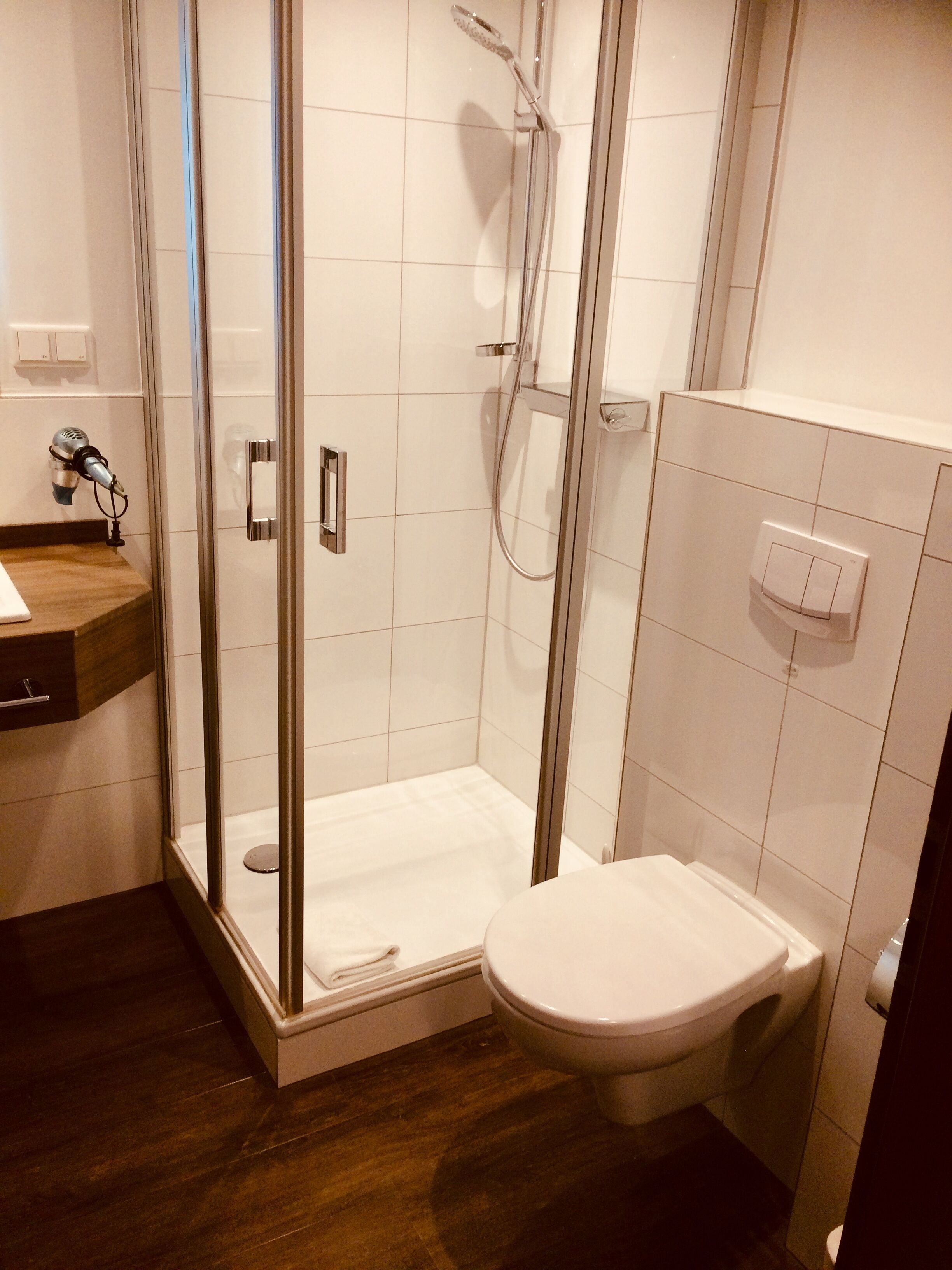 A modern bathroom with a glass shower enclosure, a toilet, and a wooden vanity with a hairdryer.