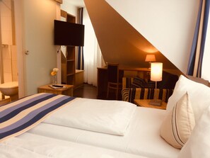 Una habitación de hotel con una cama, un televisor montado en la pared, un escritorio con lámpara y una silla.