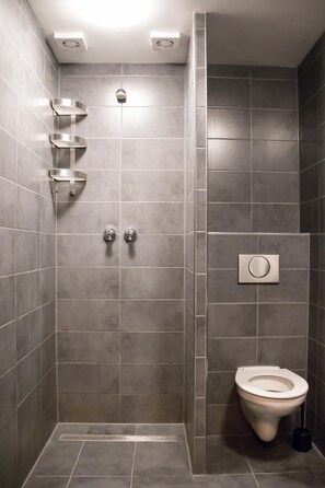 A modern bathroom with grey tiles, a shower with a wall-mounted faucet, a toilet, and a hand dryer. - Amsterdam Hostel Uptown (Amsterdam)