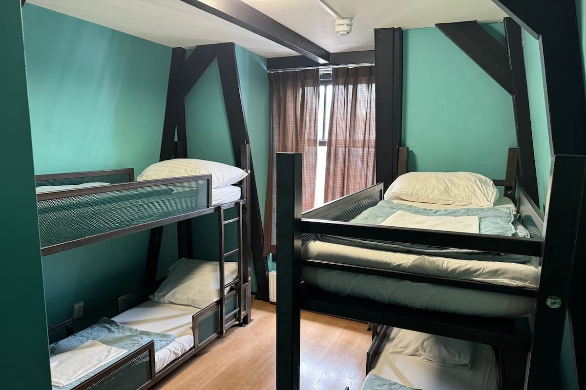 Ein Zimmer mit Etagenbetten, einem Fenster mit Vorhängen und Holzdielen.