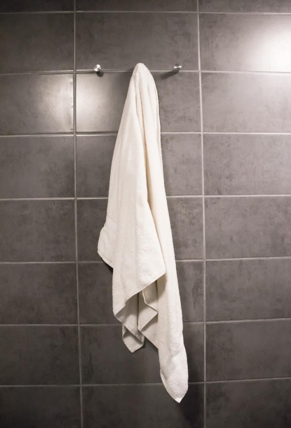 Een witte handdoek hangt aan een metalen handdoekhouder voor een betegelde muur.