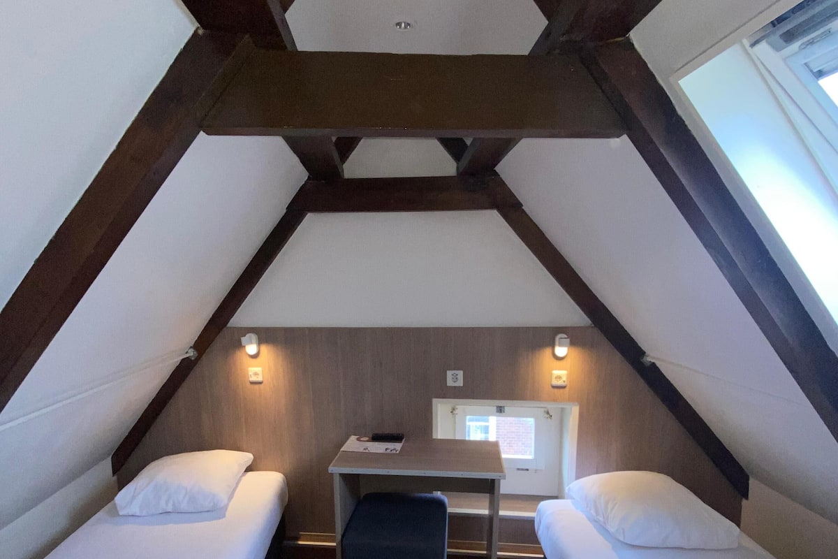 A small, cozy room with two single beds, a desk, and a window.