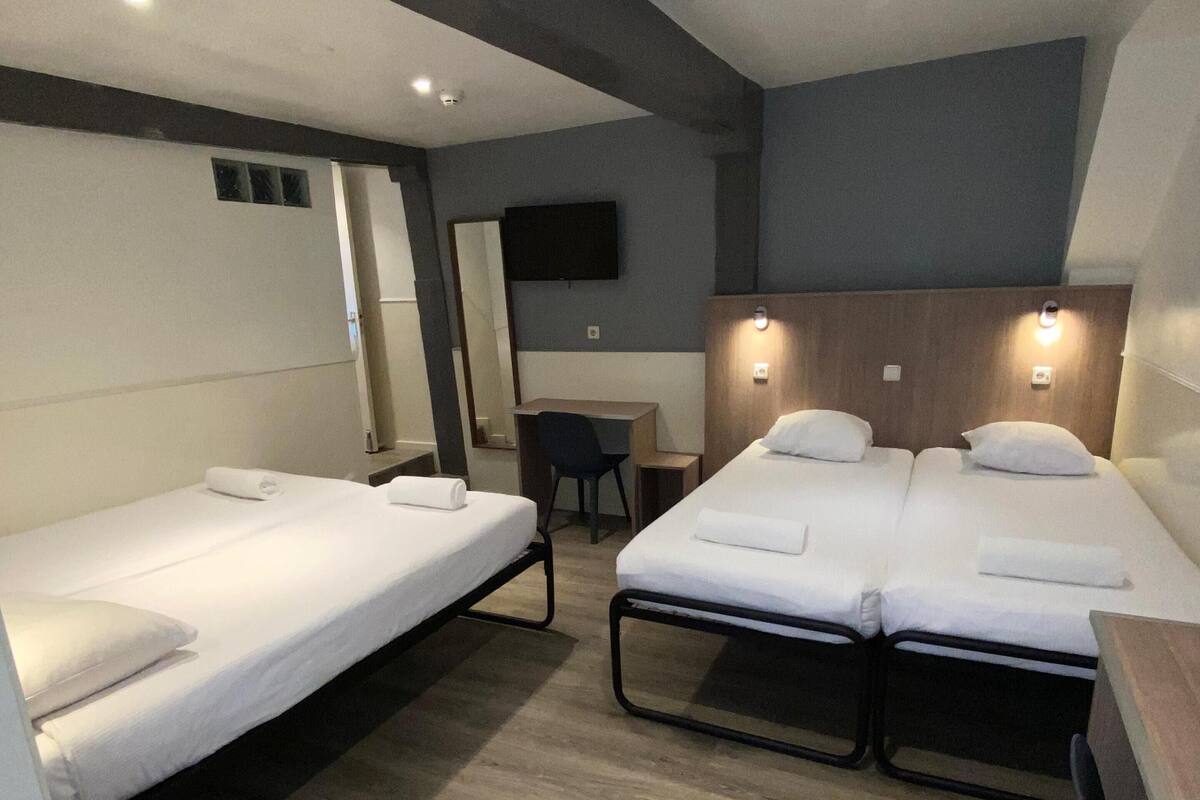 A hotel room with two single beds, a desk, a chair, a TV, and a wooden floor.