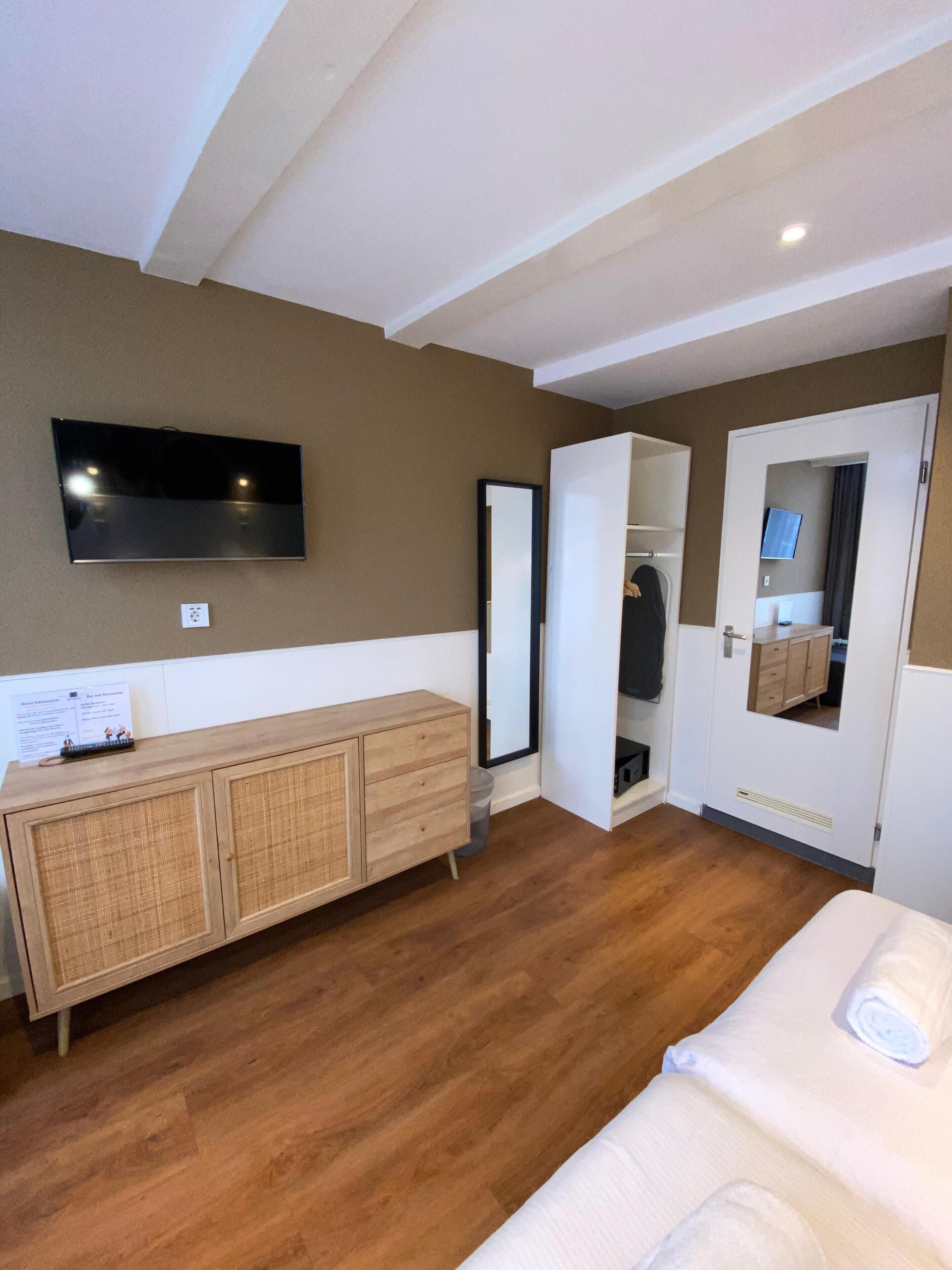 Ein Hotelzimmer mit einem Holzschrank, einem an der Wand befestigten Flachbildfernseher, einem Spiegel und einer Tür zu einem Badezimmer.