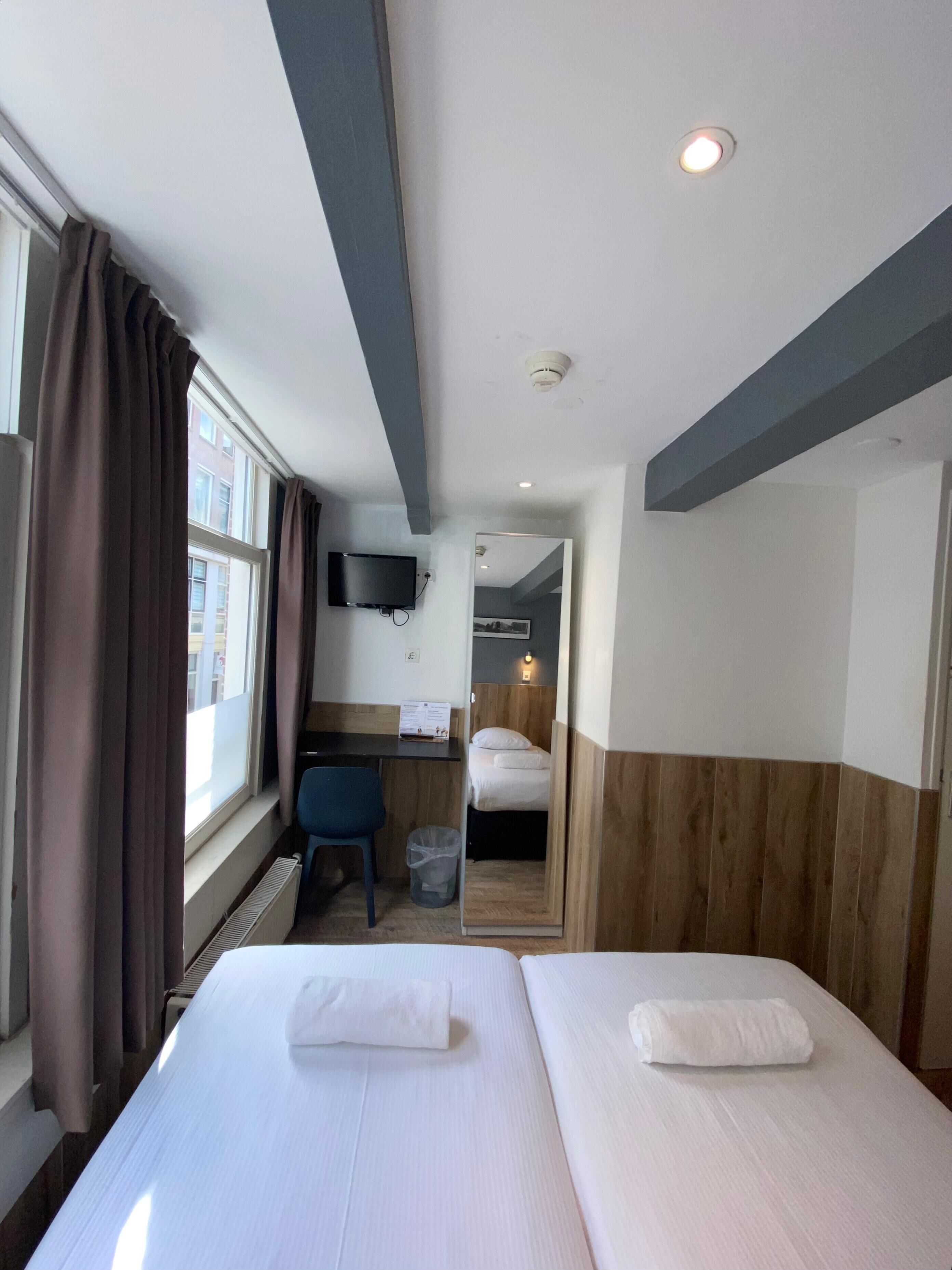 A hotel room with two beds, a desk, a chair, a TV, and a mirror.