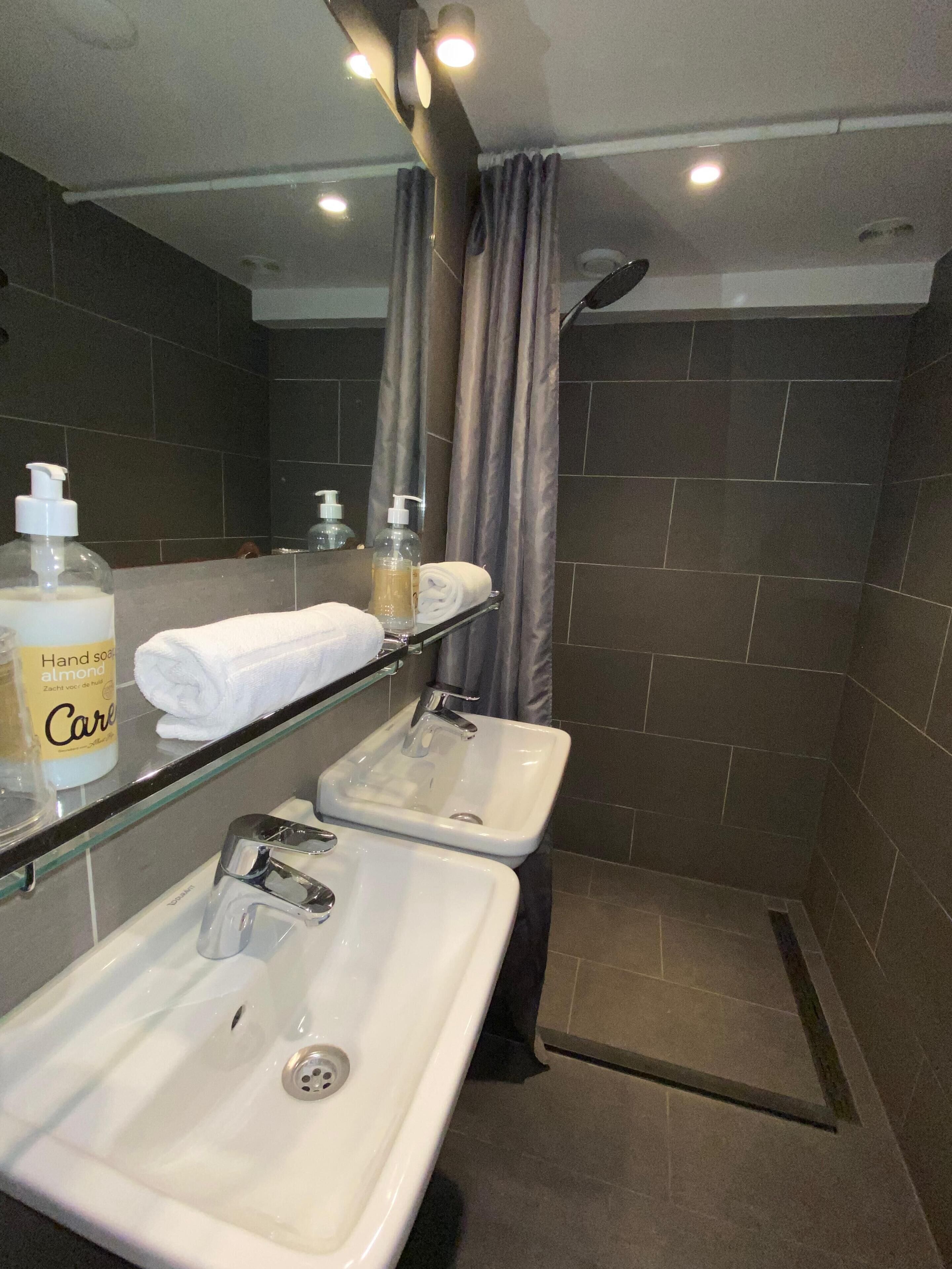 Een badkamer met twee wastafels, een douche en een glazen plank met toiletartikelen.