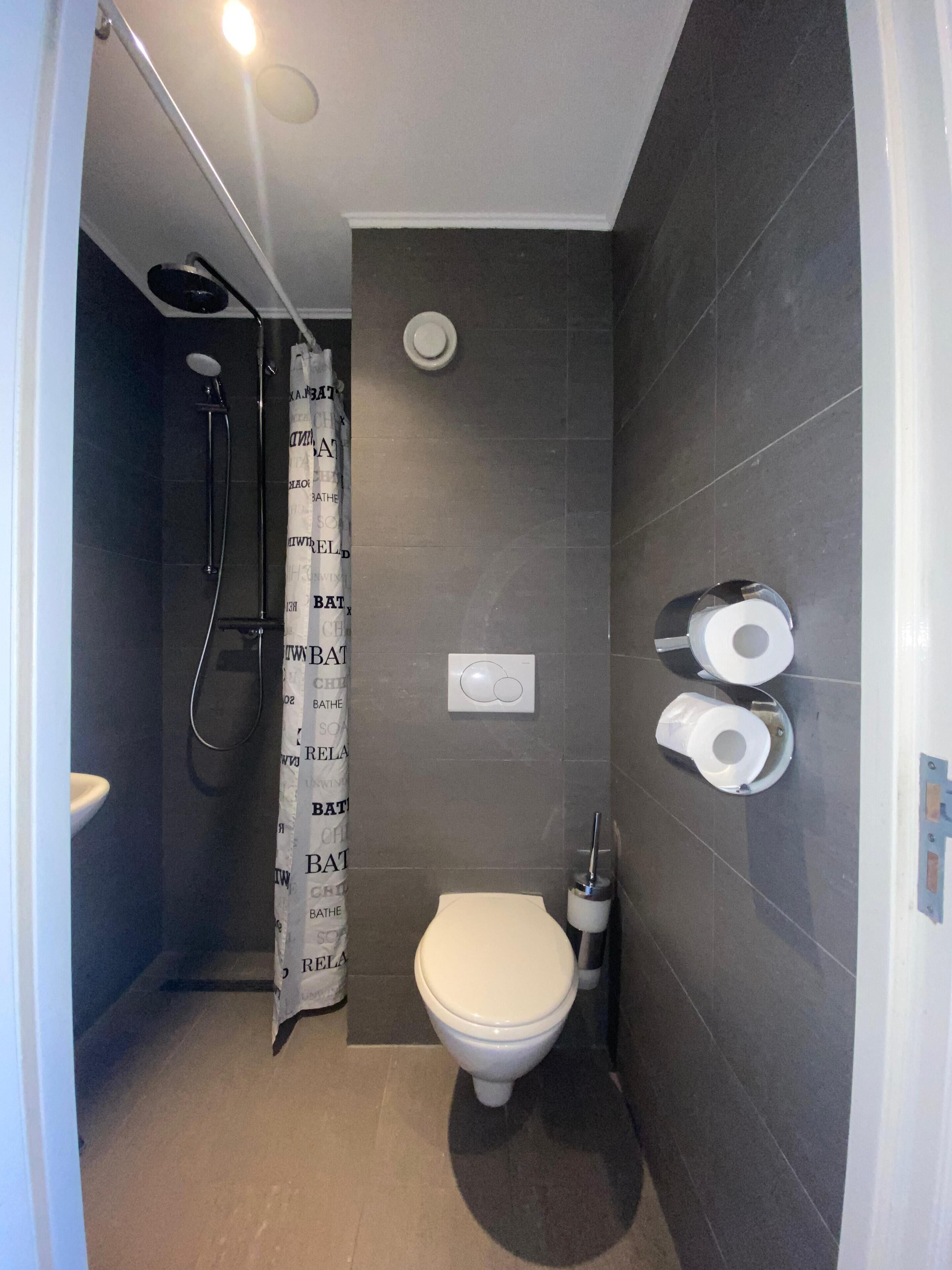 A compact bathroom with a shower, toilet, and two rolls of toilet paper on the wall.