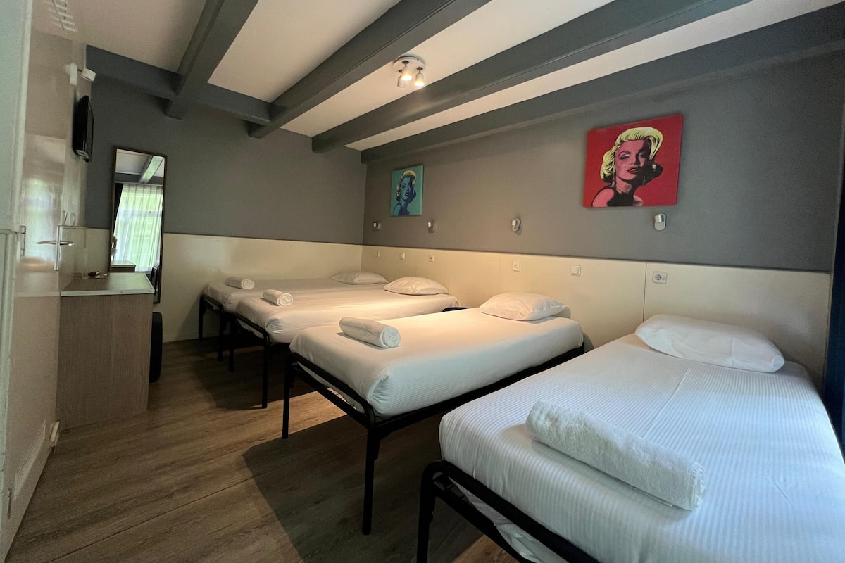 A hotel room with three beds, a small kitchenette, and a bathroom.