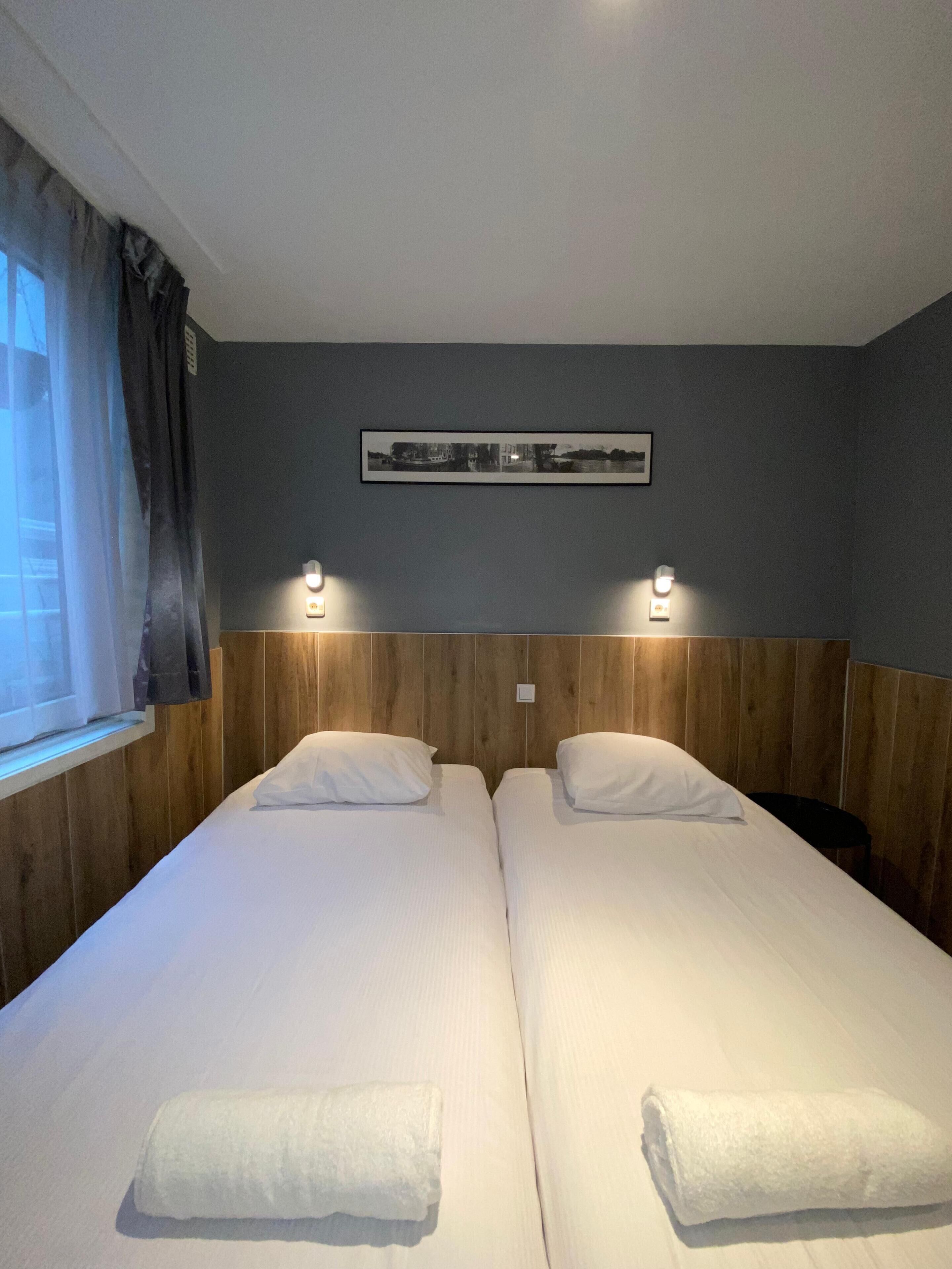 A double room with two beds, a framed picture on the wall, and two wall-mounted lights.