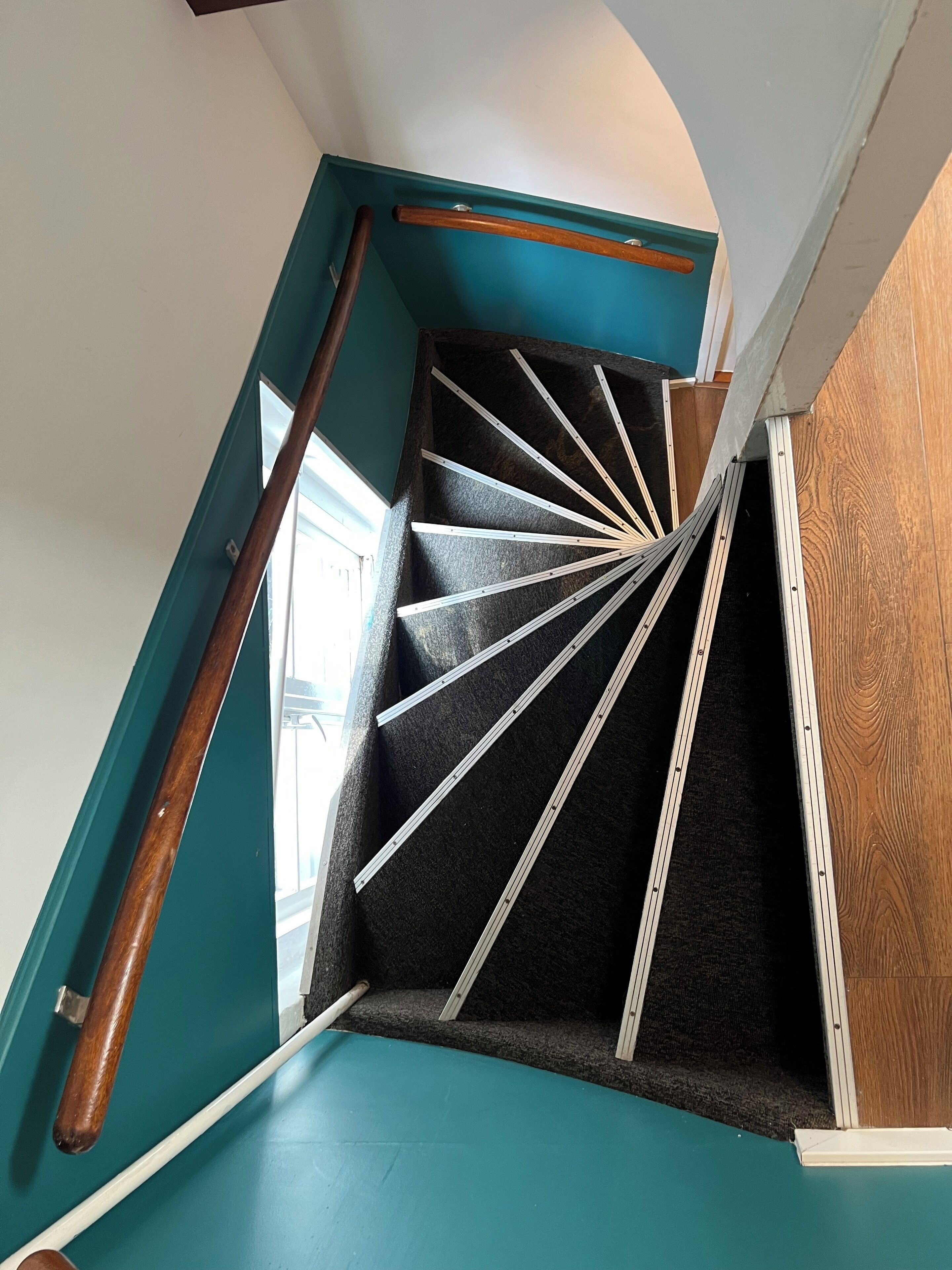 Una escalera en espiral con barandillas de madera y una pared color turquesa.
