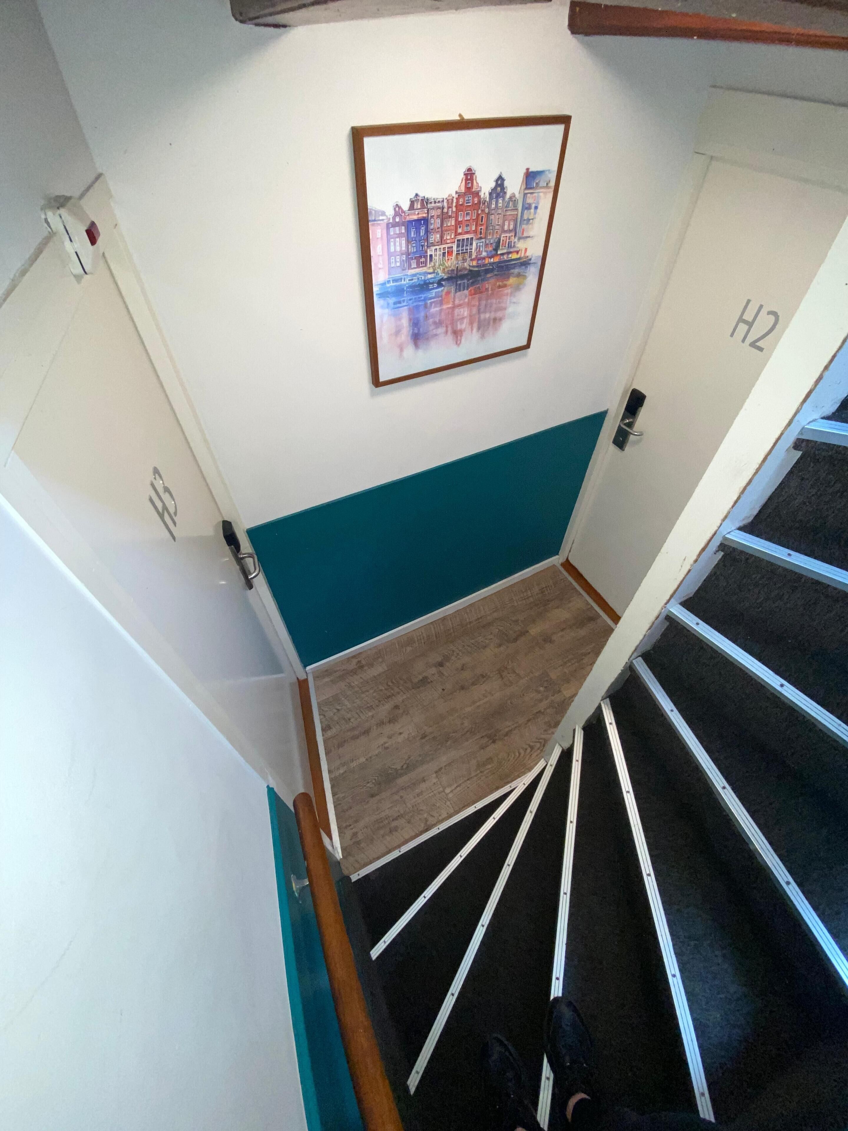 A staircase with a teal accent wall, a framed cityscape painting, and a door labeled "H2".