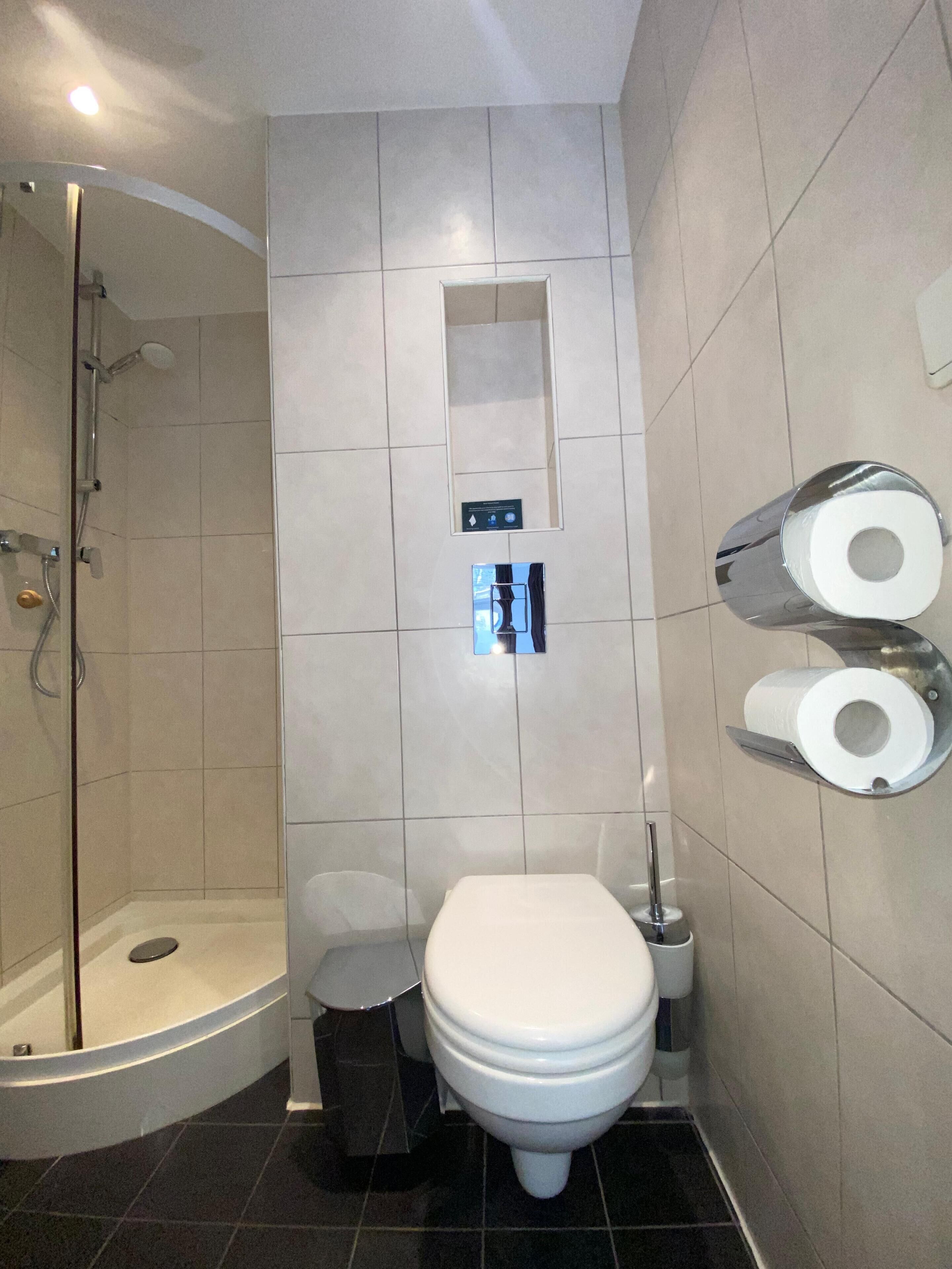 Un baño moderno con ducha, inodoro y soporte para papel higiénico.