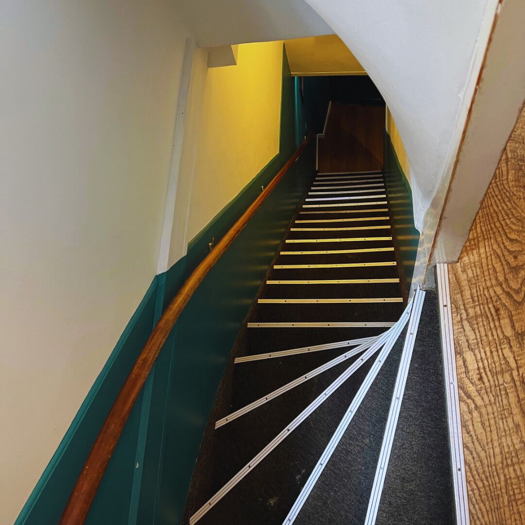 A staircase with a wooden handrail and a black carpeted floor.