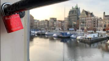 Un candado rojo con una fecha y nombres en una superficie metálica, con vista a una masa de agua tranquila con barcos y edificios al fondo.