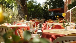 Un espace extérieur aménagé pour les repas, avec des tables recouvertes de nappes rouges et des chaises en plastique blanches.
