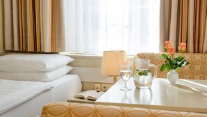 Une chambre d’hôtel avec un lit, une table de chevet avec une lampe, un vase de fleurs et une fenêtre avec des rideaux.