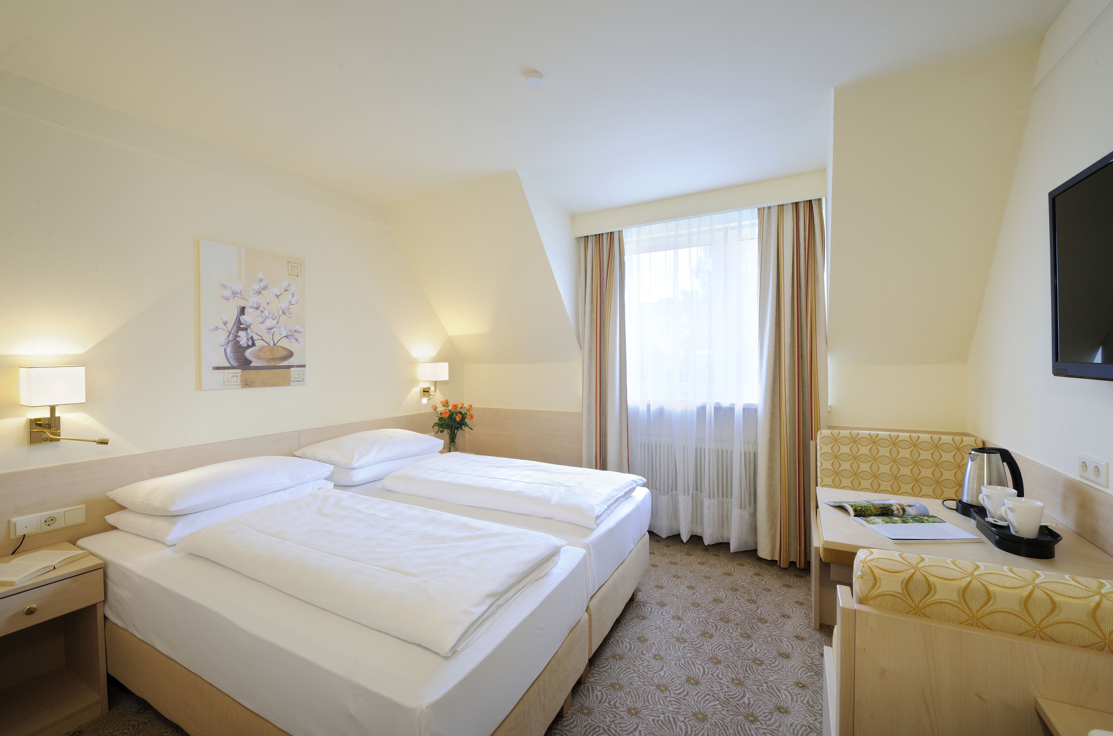 A hotel room with two beds, a desk, a chair, a TV, and a window with curtains.